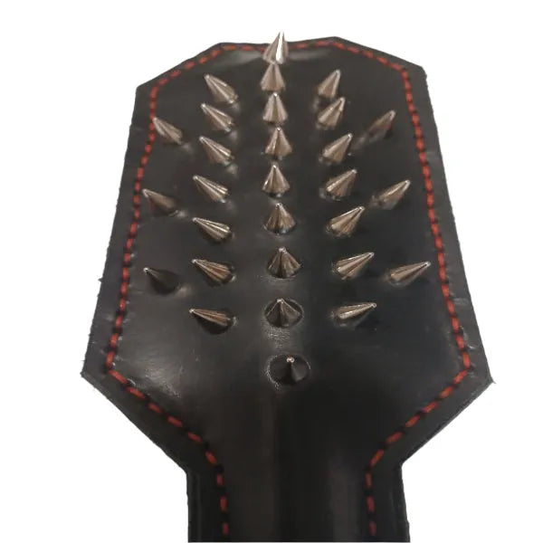 A black leather paddle with a line of metal spikes on the striking surface, featuring red stitching along the edges.
