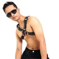 Male model wearing a black submissive-style X chest harness with buckles and O-ring detail, posing against a white background.